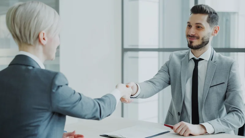 Two business professionals shaking hands across a table after an agreement